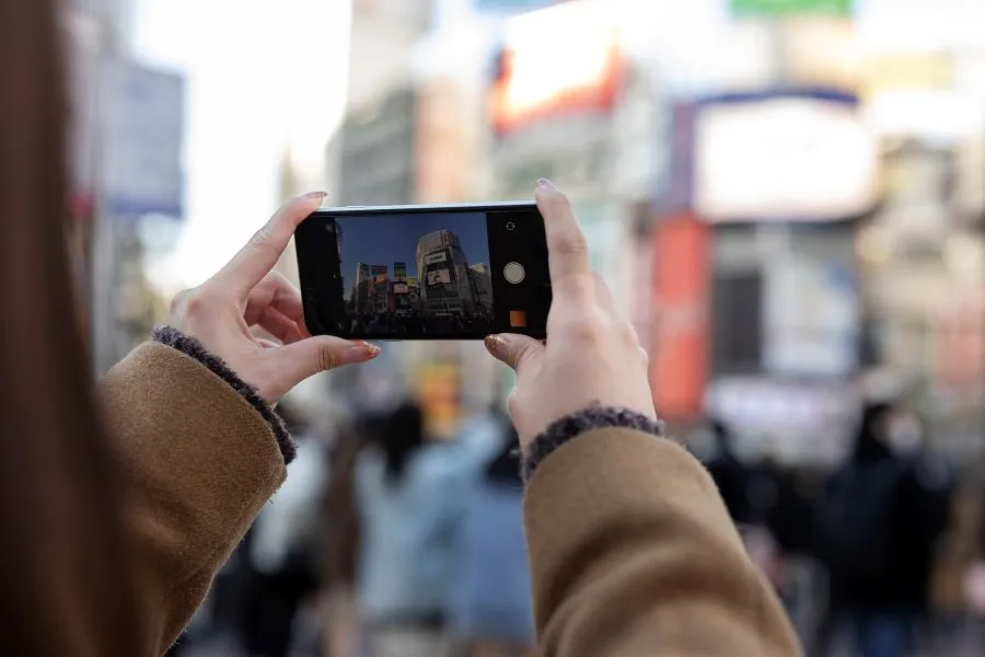 Person capturing DOOH screens in a busy city, illustrating DOOH Audience Insights in real-world environments